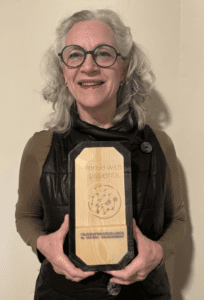 woman standing in front of beige wall holding an award.